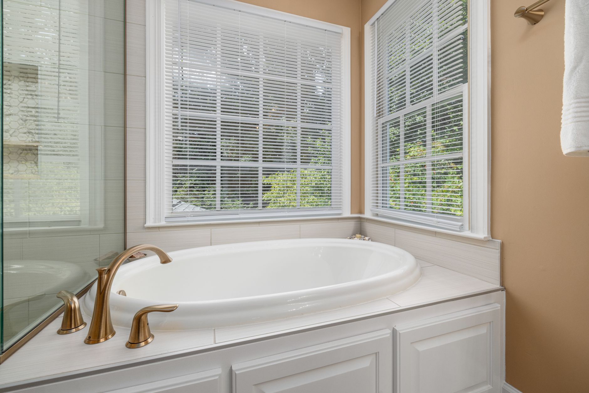 Bright bathroom featuring a white bathtub, brass faucets, and large windows with blinds in Riverside, CA